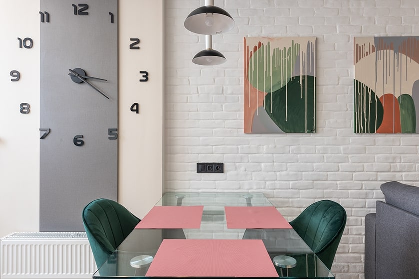 Esszimmer mit 2 großen Bildern, einer Uhr, einer weißen Steinwand und grünen und rosa-farbigen Akzenten