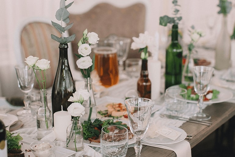 Gedeckter Tisch mit Gläsern, Karaffen und Blumensträußen 